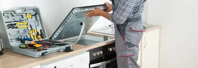 Cooktop repair technician lifting a built-in stovetop for service in Saint Petersburg, FL